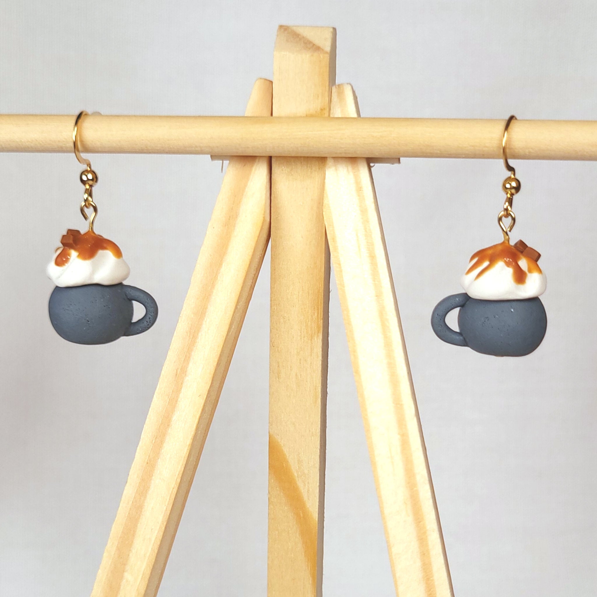 Earrings shaped like small coffee mugs with whipped cream and caramel sauce on top